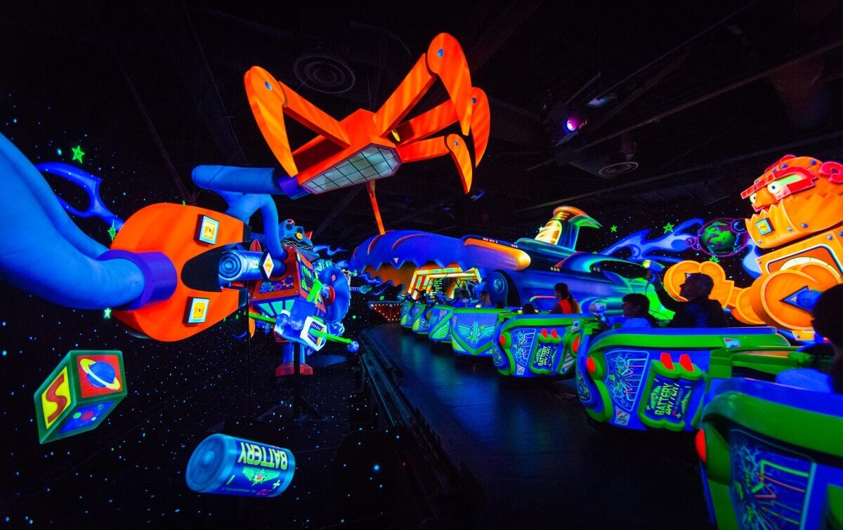 Interior design the cars of Buzz Lightyears Laser Blast drive in a row one after the other through scenes in neon colors