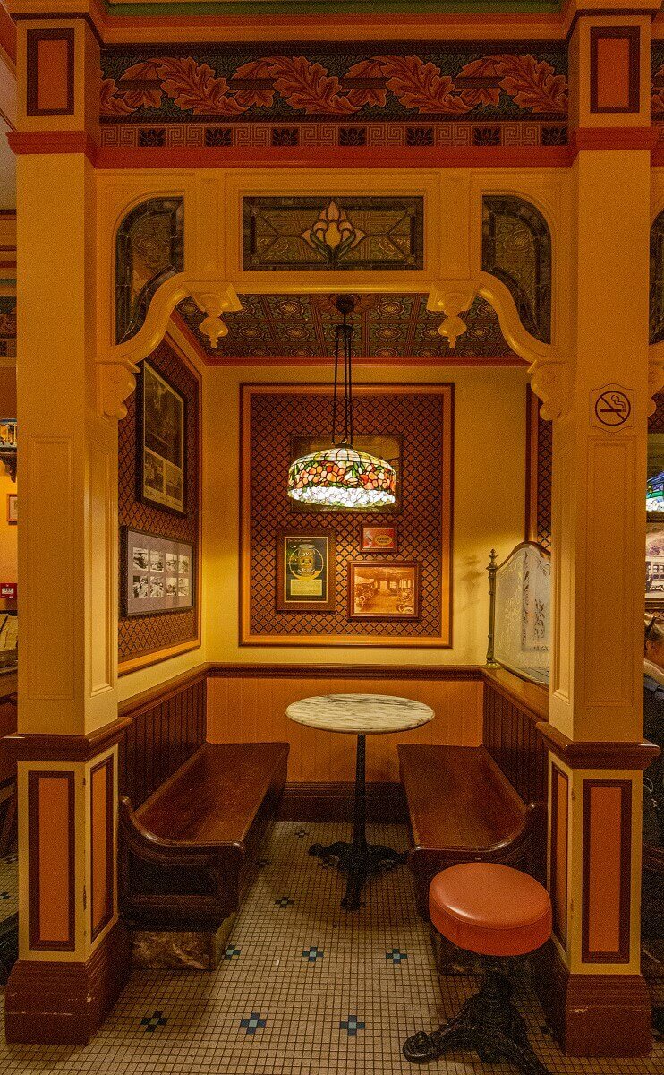 A niche in the guest room One of the niches in the restaurant's dining room. To the left and right are wooden benches, in the middle a table over which hangs a hanging lamp made of stained glass, and behind it on the wall historical photos.