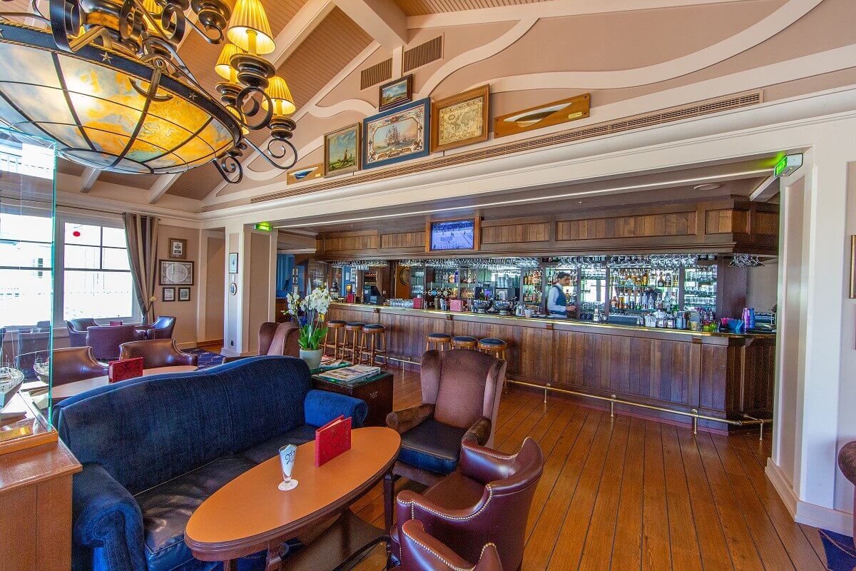 Captain Quarters Bar View of the bar in maritime style. In front of the bar are leather armchairs, and benches under the chandelier. Above the bar hang pictures.
