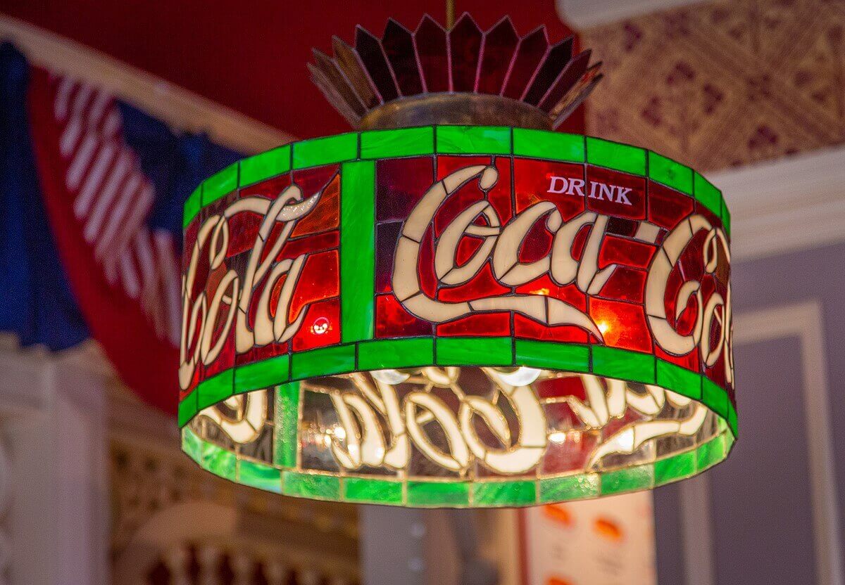 A Coca Cola lamp in detail A Coca Cola lamp in detail. The round lamp is assembled like a mosaic of white, green and red slices of stained glass. Its edges are green, the surface red and in it is 3x the lettering Coca-Cola
