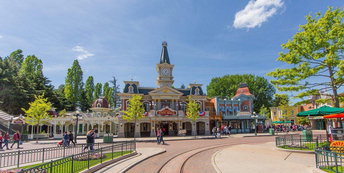 Wide shot of City Hall Long shot of City Hall, with the Aboretum to the left and the Storybook Store to the right. In the middle of the building with red facade and blue roofs is a classic clock tower.