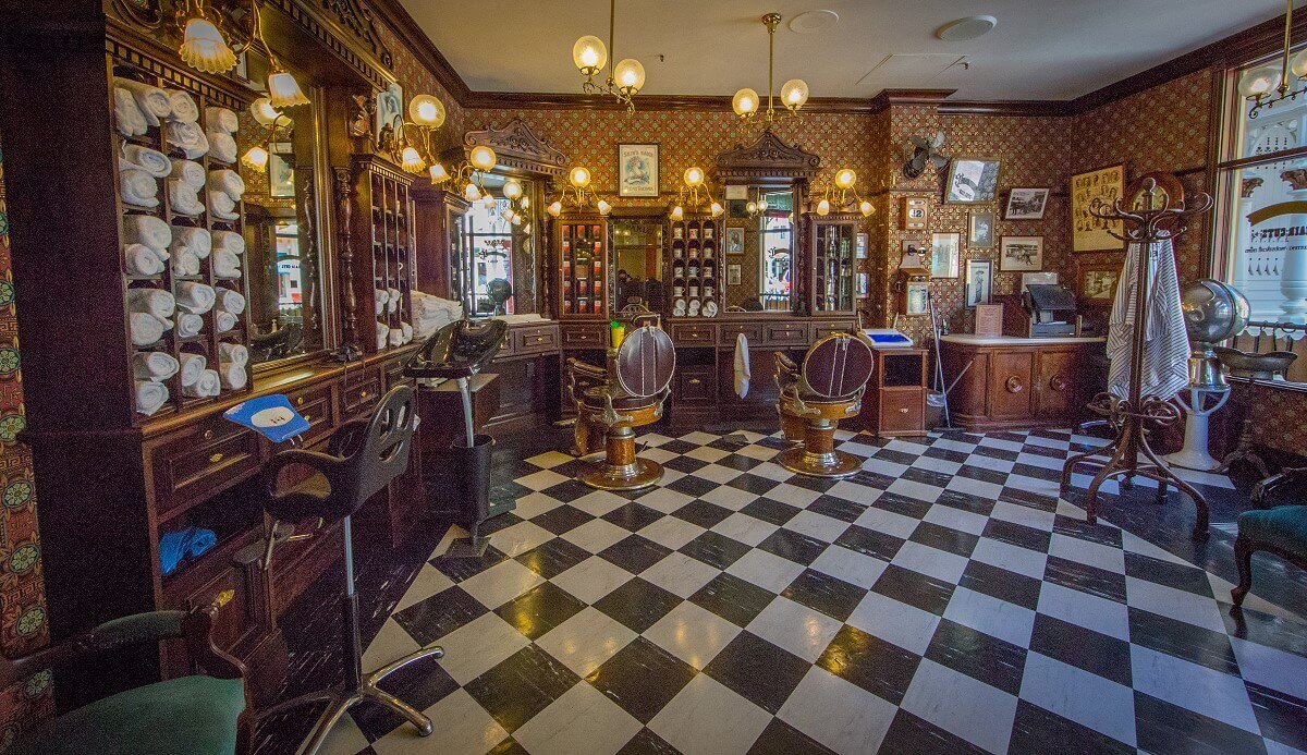 Dapper Dan's Hair Cuts The entire space of Dapper Dan's Hair Cuts. The floor is tiled with black & white tiles in a diamond shape, the furnishings are classic brown, and the clients' chairs are brass with brown leather upholstery.
