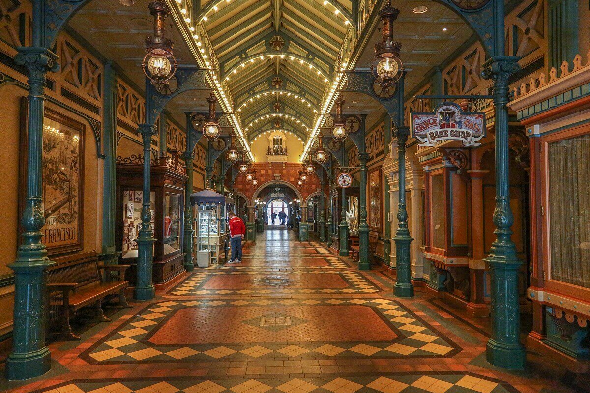 Wide shot of the Discovery Arcade, about halfway up the walkway. Wide shot of the Discovery Arcade, about halfway up the path. On the right the entrance to the Cable Car Bake Shop, the arcade is covered by a roof with green painted beams, on the left pictures and showcases.