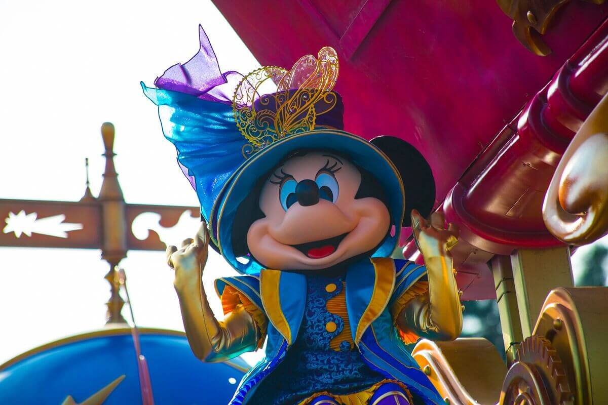 Minnie Mouse with big hat Minnie mouse wears a blue-gold outfit and long golden gloves, plus a huge hat in blue-purple with big golden decoration