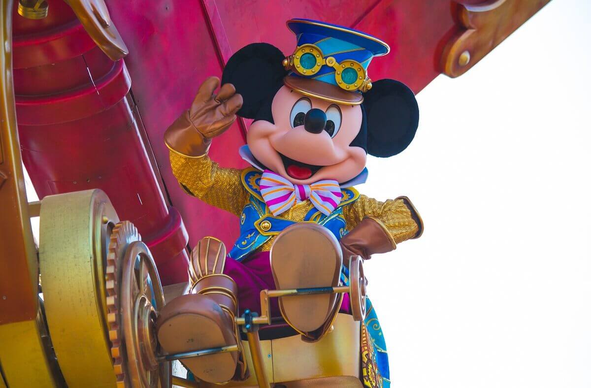 Mickey mouse greets Mickey Mouse is wearing a blue hat with a brown visor, on which he has clamped a pair of gold aviator glasses. He has raised his right hand in salute