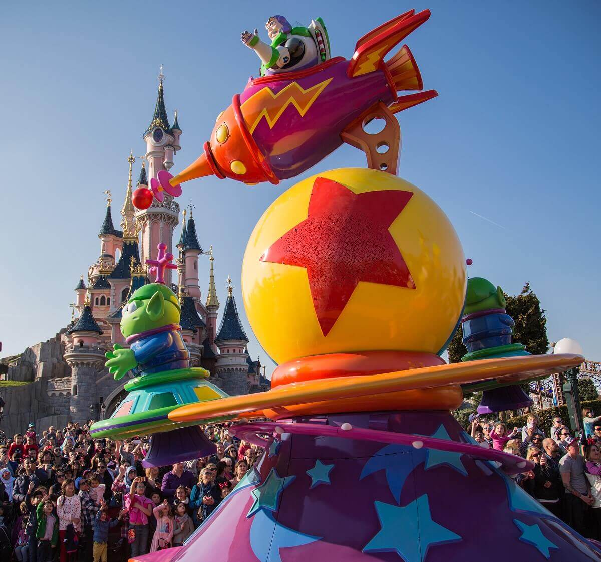 Space vehicles at the parade Toy Story floats at Disney Stars in parade in front of Sleeping Beauty Castle. Buzz Lightyear in a rocket hovering over the Pixar Ball and two green aliens in flying saucers.