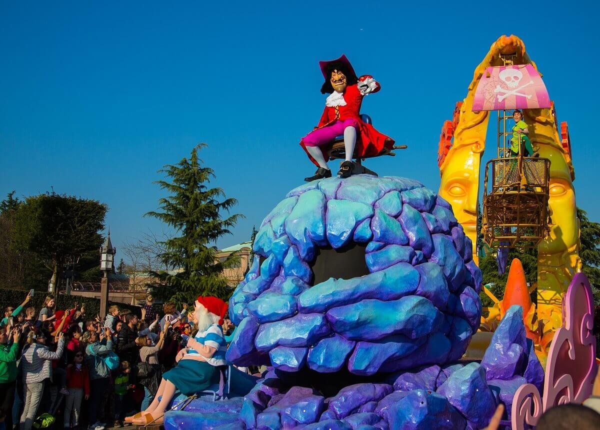 Captain Hook on the parade float Captain Hook sits on a giant skull rock, Smee sits at his feet, they are followed by Peter Pan in a flying ship.