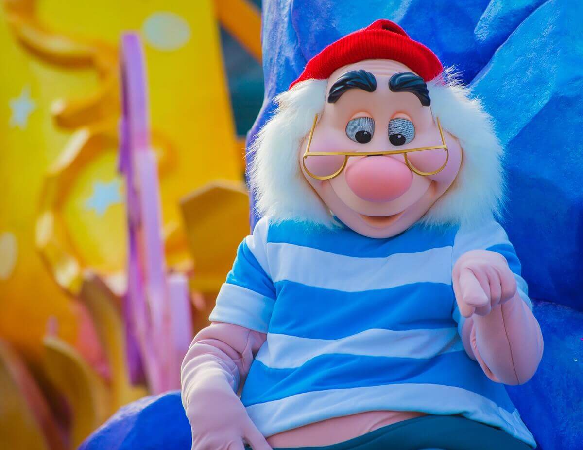 Smee points to the audience Smee sits on the parade float and looks down slightly, he points his hand at the spectators
