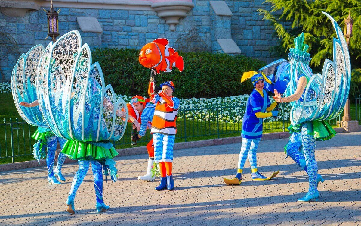 Underwater scene at the parade Two dancers with clown fish figures and a dancer with a dory figure in her hand, around them dancing water plants