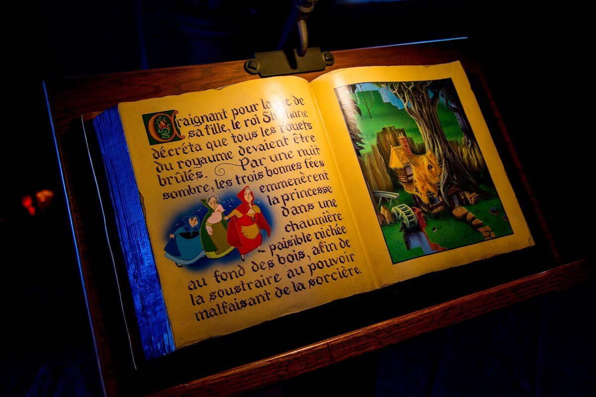 Open storybook On a wooden desk lies an open storybook with a picture of the three fairies and a hut in the forest