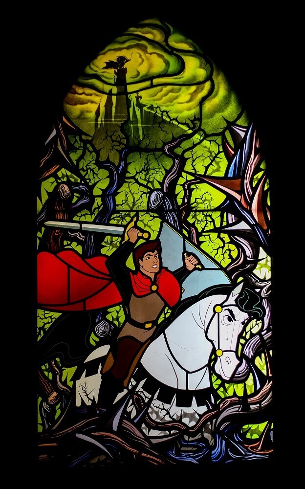 Stained glass window with fighting prince A stained glass window shows a prince on a white horse armed with a sword making his way through the thorny bushes