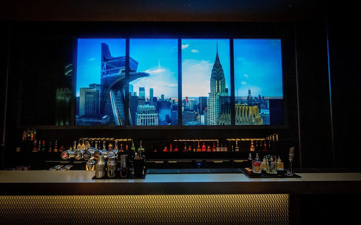 Skyline Bar The counter of the Skyline Bar with various utensils, bottles, in the background an illuminated picture of New York in shades of blue.