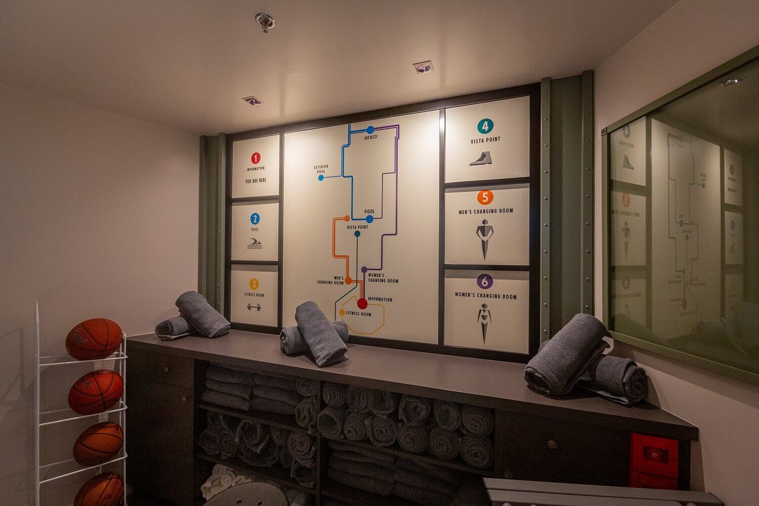 Map of the fitness and pool area A signpost of the pool and fitness area, underneath is a shelf with gray towels