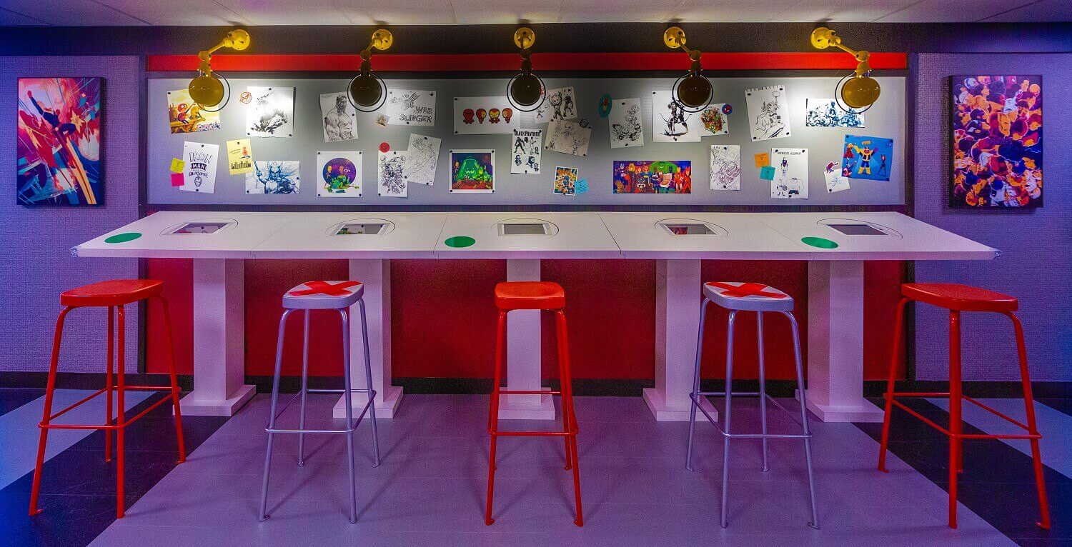 Drawing table in the Marvel Design Studio A large drawing table in the Marvel Design Studio with five stools and lamps on the ceiling.