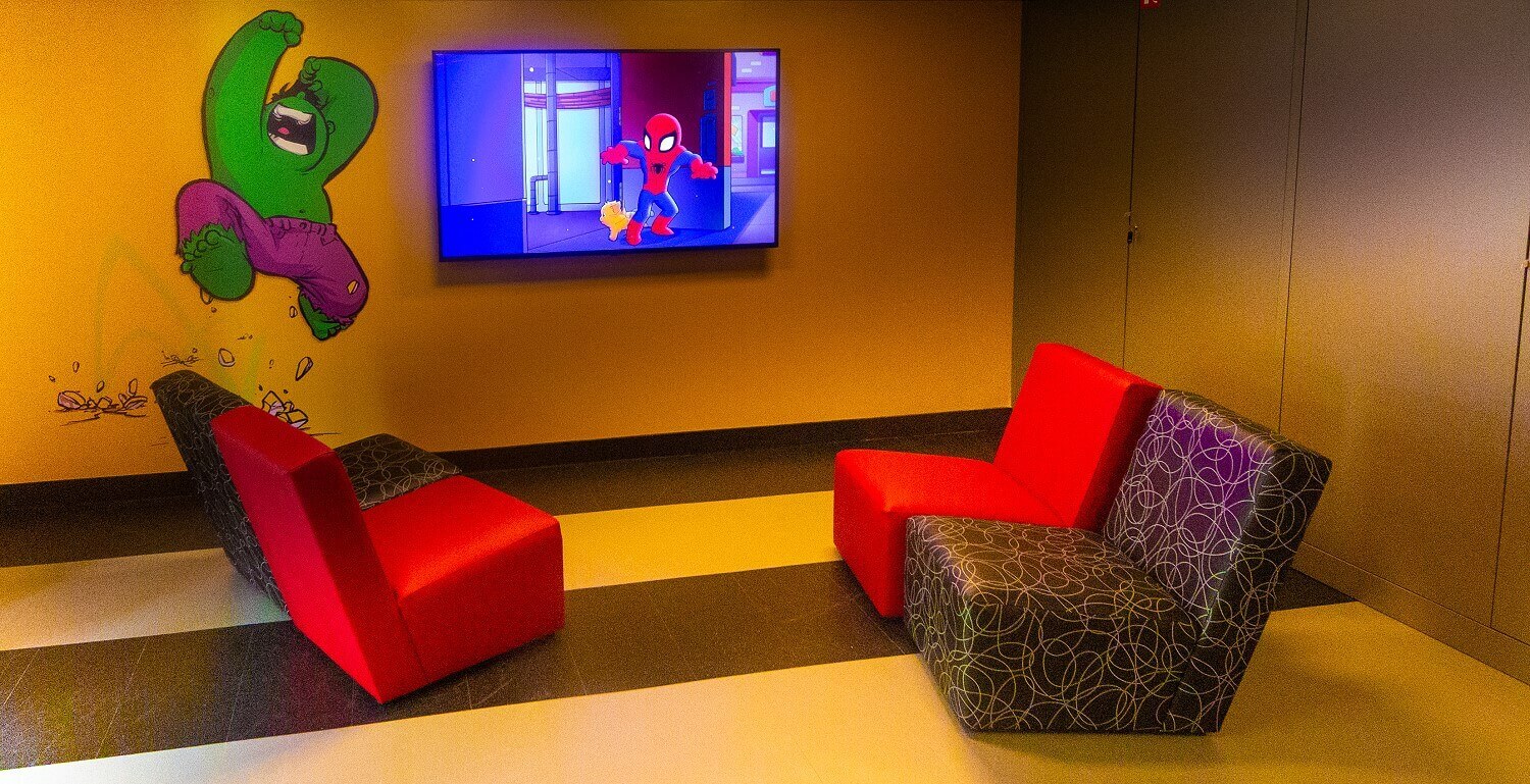 Lounge corner in the Marvel Design Studio There are four armchairs in a lounge corner in the Marvel Design Studio. A Spiderman comic is playing on the TV on the wall.