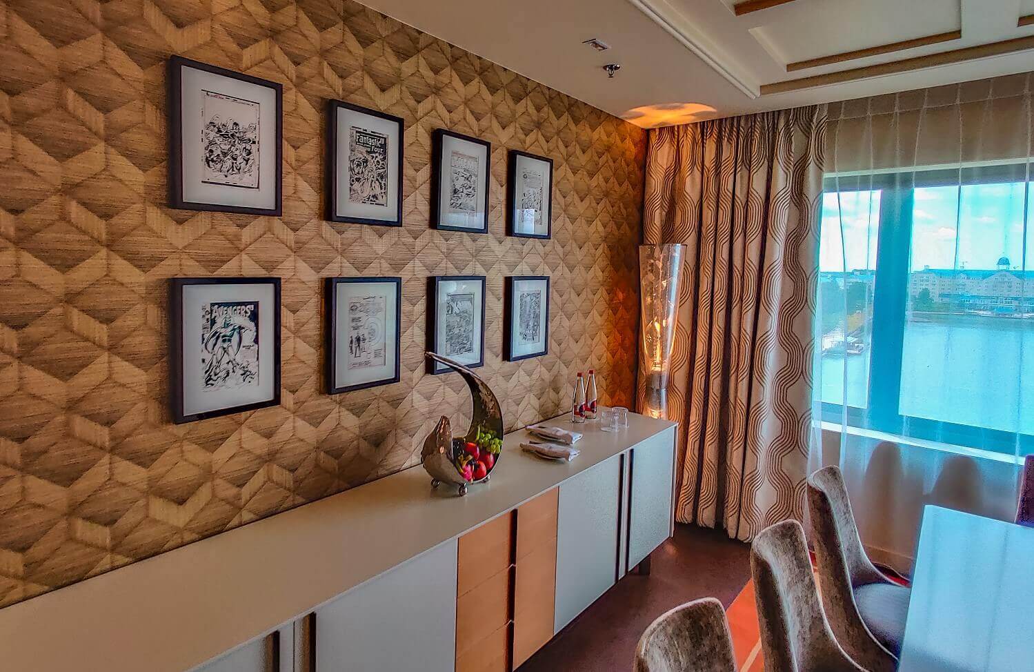 Presidential suite seating area A sideboard with a bowl of fruit on it, next to it is a modern lamp, and pictures hang on the wall