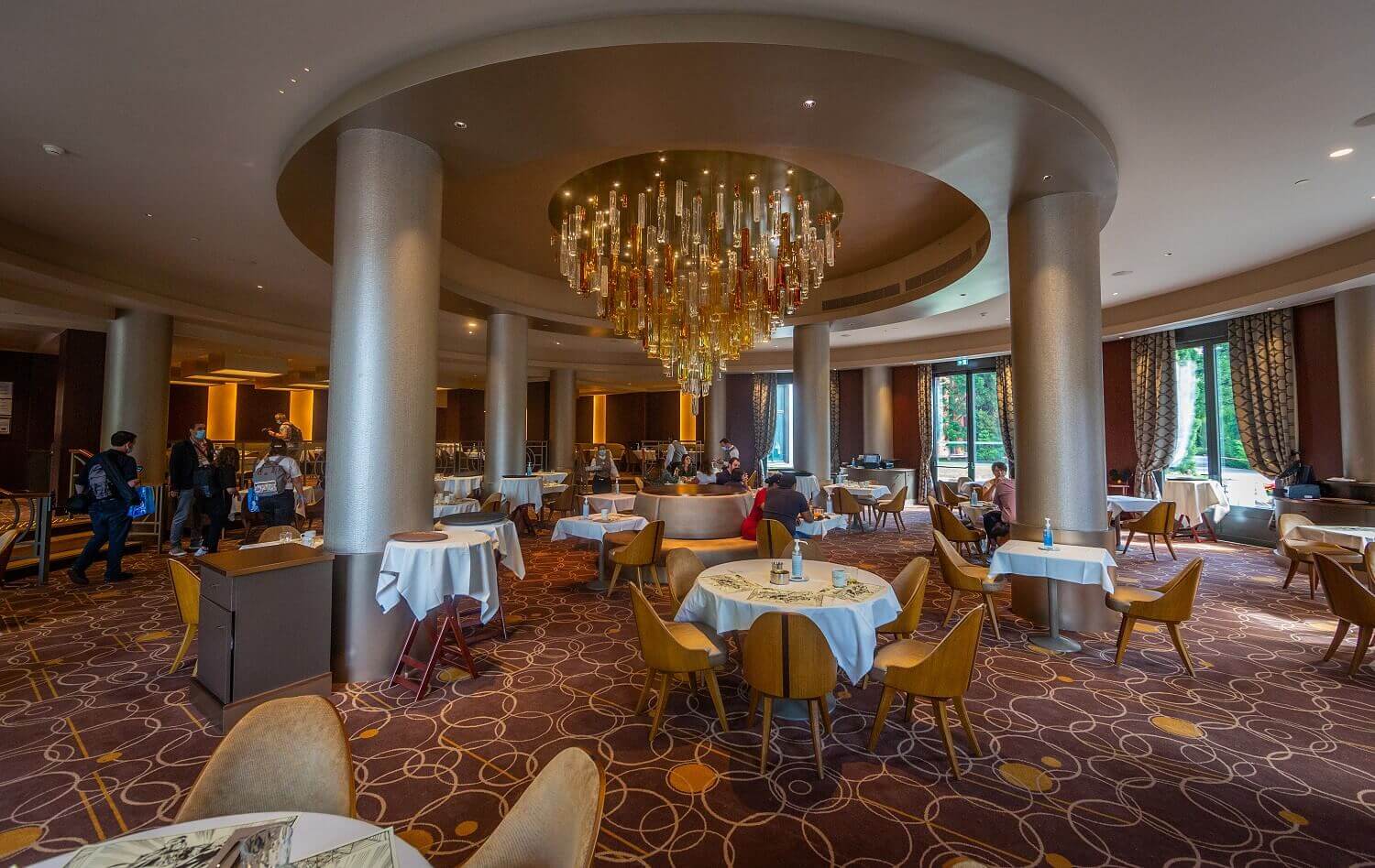 Manhattan Restaurant Tables with white tablecloths stand under the large central chandelier, which is surrounded by massive columns.