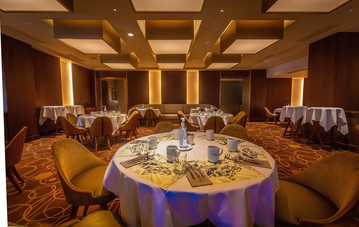 Manhattan Restaurant Several large round tables are set for the breakfast buffet. The room has a warm atmosphere due to the indirect light.