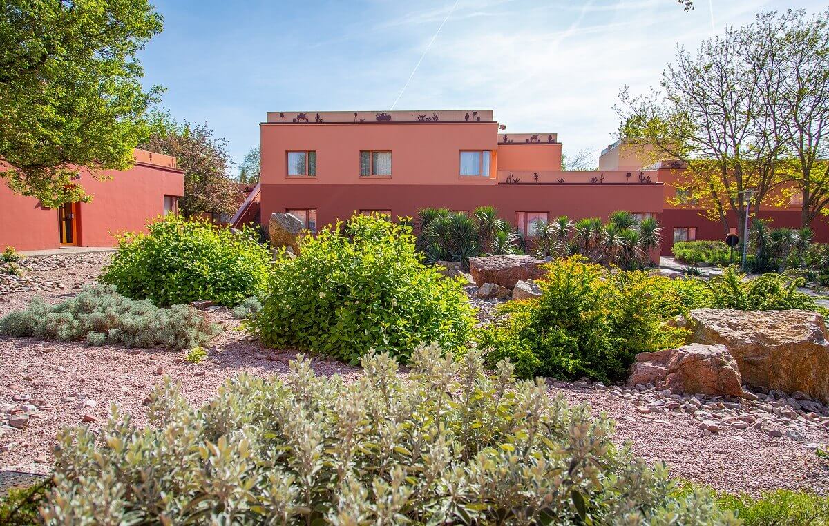 Santa Fe Hotel Building A small gravel garden with cactus palms, shrubs, trees and boulders. Behind it hotel buildings.