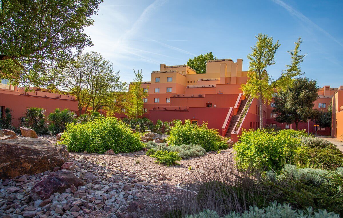 Santa Fe Hotel Building A small gravel garden with cactus palms, shrubs, trees and boulders. Behind it hotel buildings.