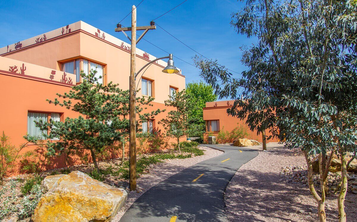 Santa Fe Hotel Building with Route 66 In addition to Route 66, there are trees, rocks, a streetlight, and a hotel building.