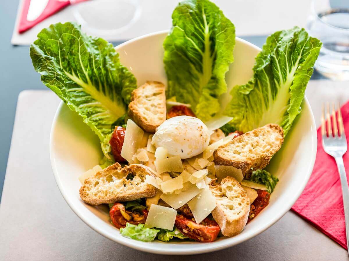 Lettuce A plate of salad: romaine lettuce leaves, dried tomatoes, pieces of bread, parmesan cheese and a soft egg.