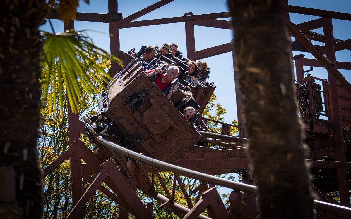 Carriage in full swing at Indiana Jones et le Temple du Peril View past trees to a fully occupied car of the Indiana Jones roller coaster