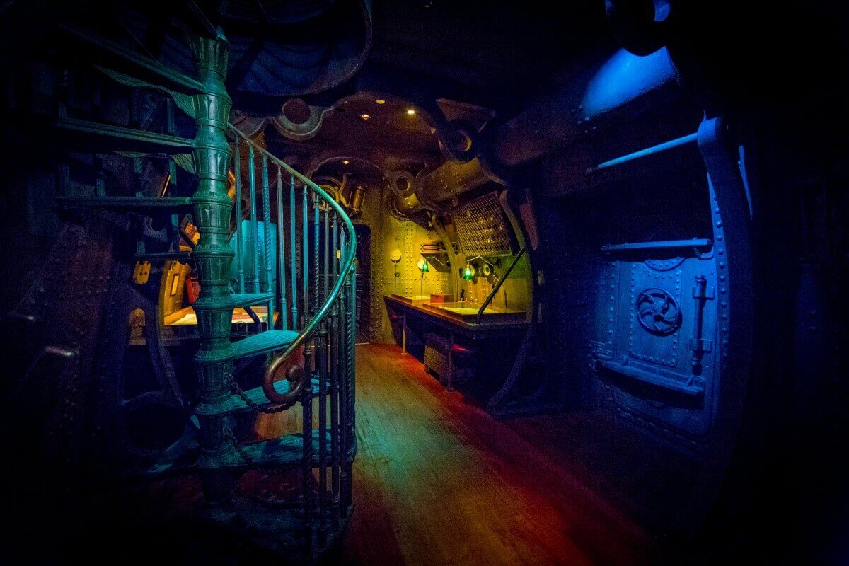 Room inside the Nautilus View of a poorly lit room with an iron spiral staircase and a card table inside the Nautilus.