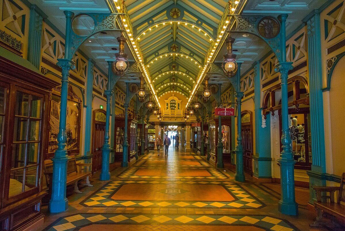 Wide shot of the Liberty Arcade Long shot of the Liberty Arcade. Wrought iron green columns hold the ceiling, to the right and left along the arcade are display cases, pictures and benches along the walls and the floor is tiled with white, green and brown tiles.