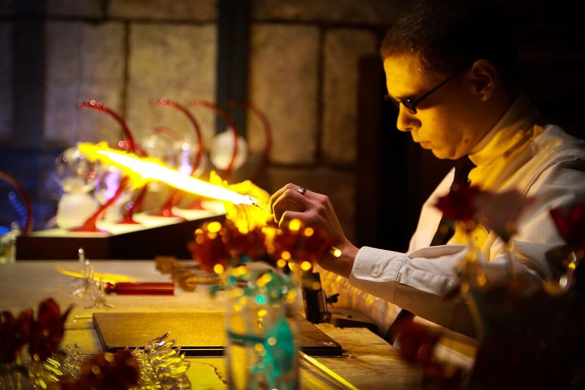 Glass blower at work A glassblower wearing protective goggles works on a filigree souvenir made of glass