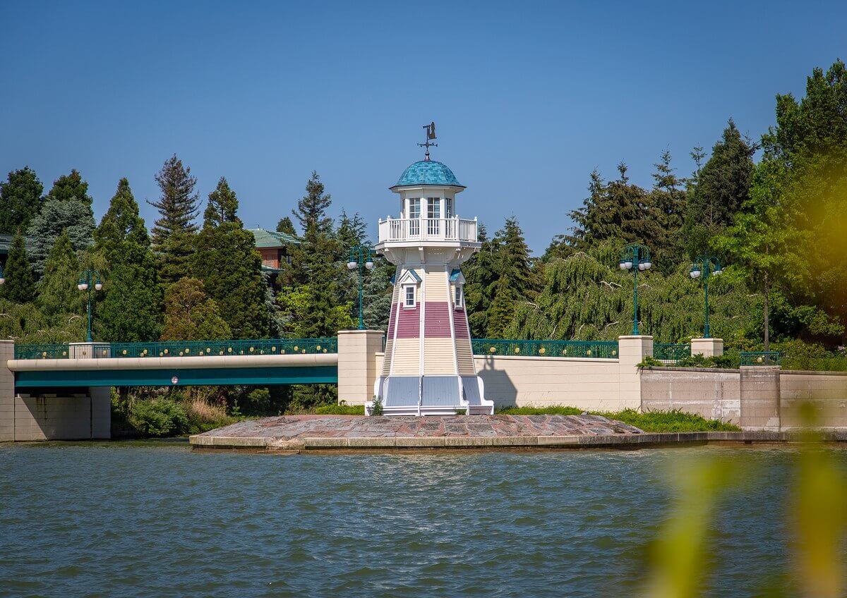 Lighthouse Hotel Newport Bay Club A small lighthouse with blue, white and red stripes stands on the edge of the shore in front of the New Port Bay Club hotel.