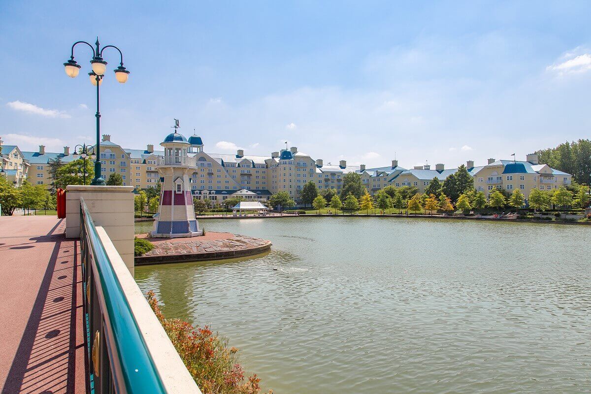 Lighthouse Hotel Newport Bay Club A small lighthouse with blue, white and red stripes stands on the edge of the shore in front of the New Port Bay Club hotel.