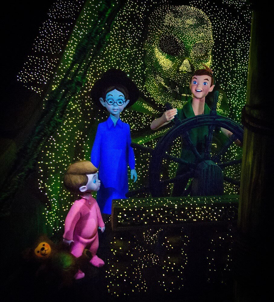 Peter Pan steers the ship Peter Pan stands next to John and Michael Darling at the helm of the sparkling pirate ship at the end of the Peter Pan's Flight attraction