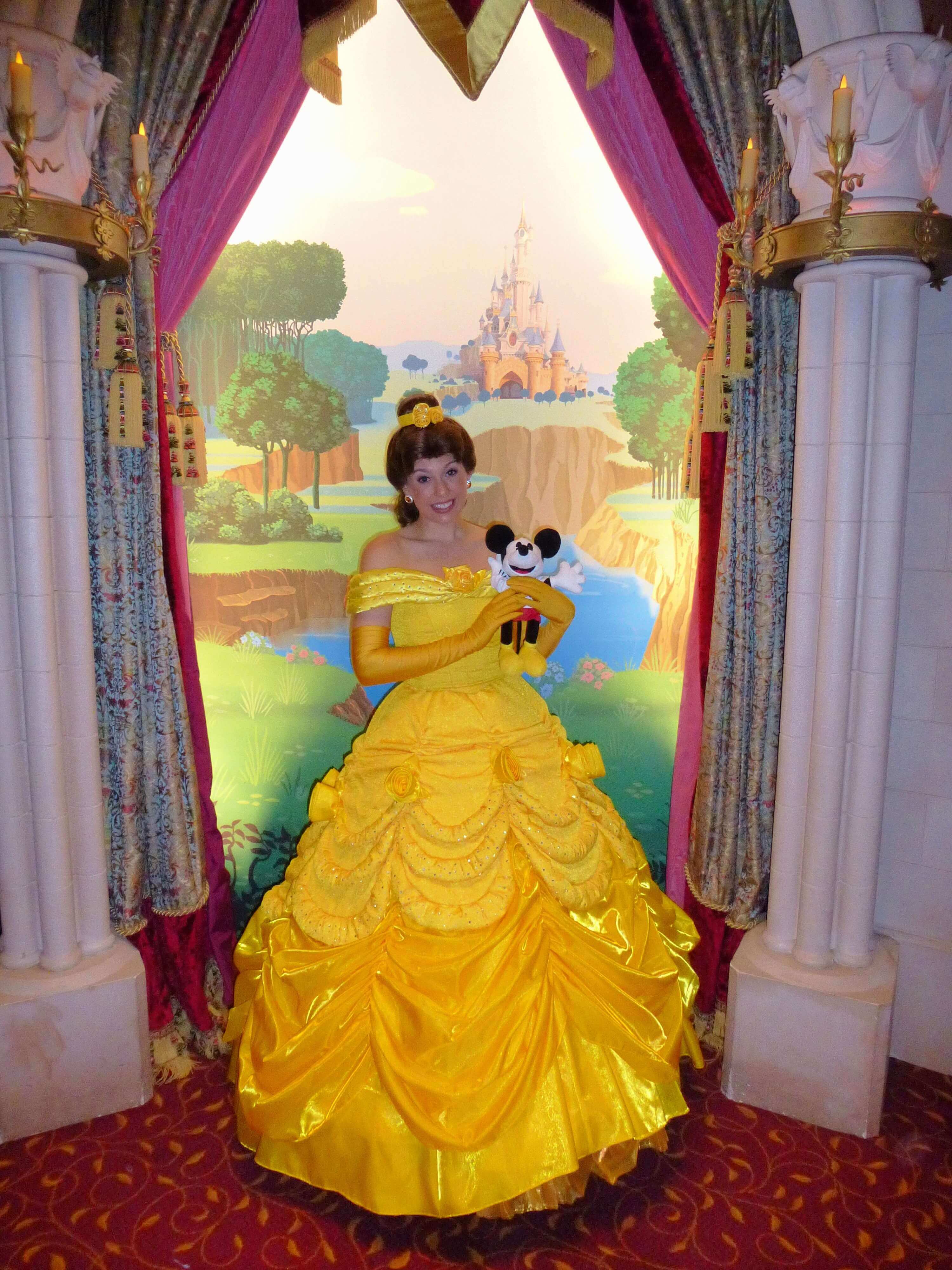 Belle in princess pavilion Belle poses with a plush figure in the shape of our dein-dlrp mascot in her arms for a photographer in the princess pavilion