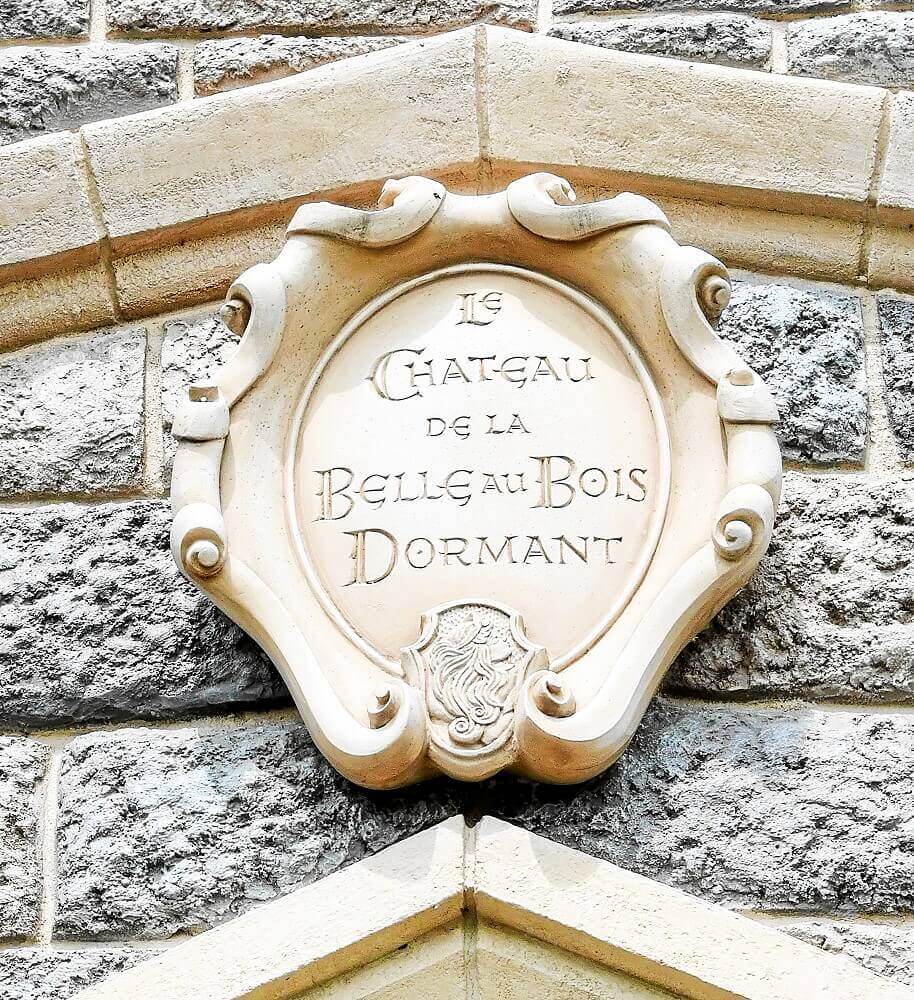 Sign above the entrance on a coat of arms-shaped sign above the entrance to the Sleeping Beauty Castle, the words La Chateau de la Belle au Bois Dormant can be read