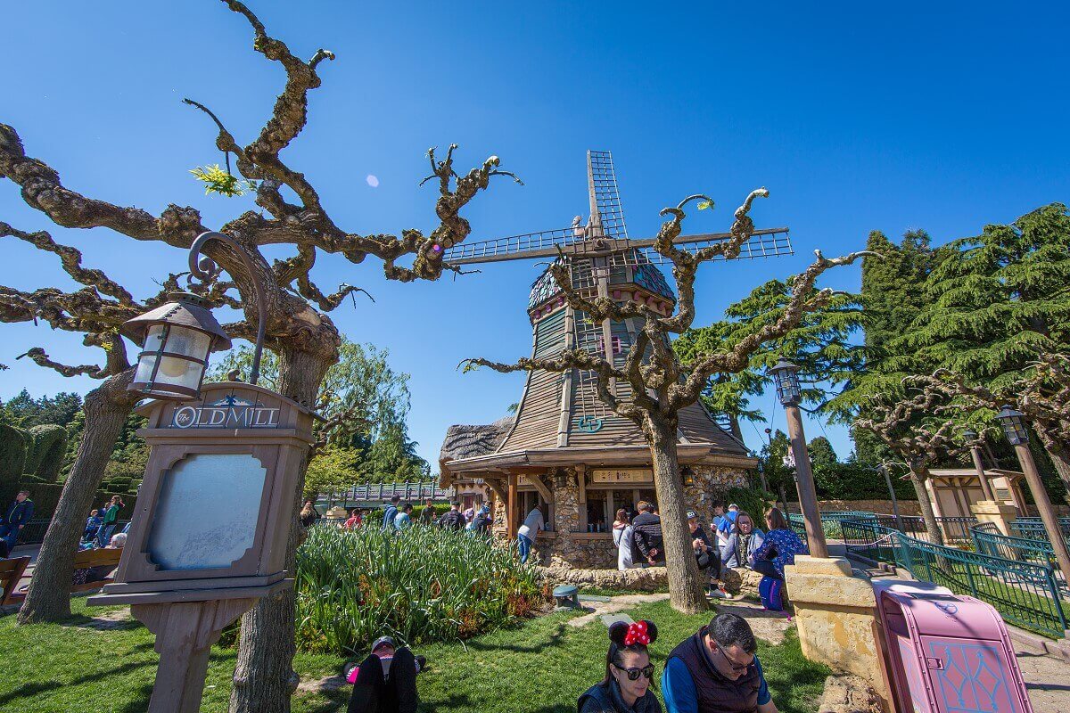 Snack bar The Old Mill in Fantasyland View past green areas and trees to the snack bar The Old Mill in the shape of a wooden windmill