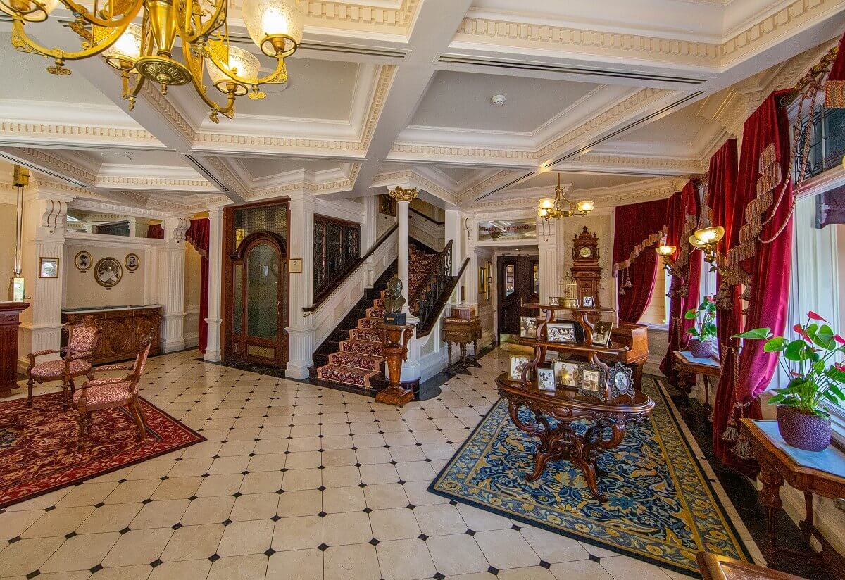 Foyer on the ground floor of Walt's - An American Restaurant Foyer on the ground floor of Walt's - An American Restaurant. The elegant room is brightly tiled, to the right are windows with heavy brocade curtains, in the middle a table with numerous framed black and white pictures of Walt Disney and a staircase and elevator leading to the dining rooms